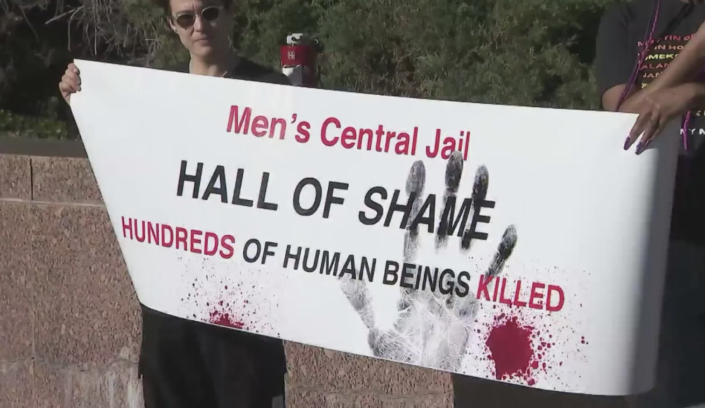 Image of a banner saying "Men's Central Jail, Hall of Shame, Hundreds of Human Beings Killed" with blood spatters and hand prints on it.